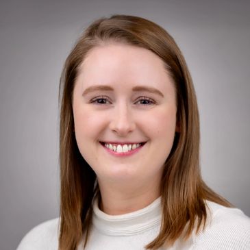 Smiling woman with light brown hair in a white top against a gray background.