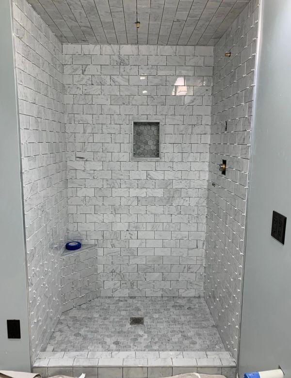 Newly tiled white marble shower with bench and niche.
