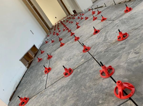 Floor tile leveling system with red spacers and black wedges.