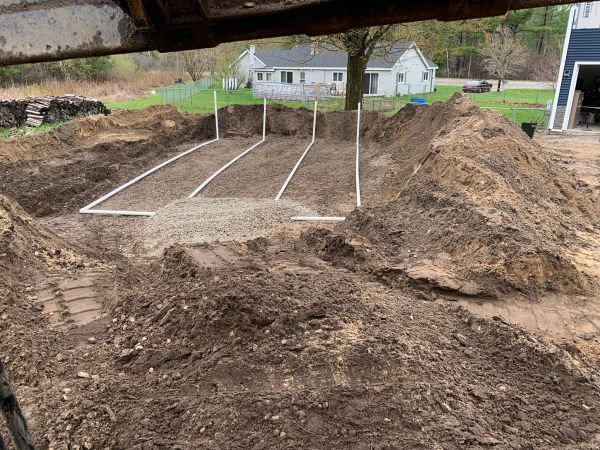 Trenches with pipes being laid in a soil excavation near houses.