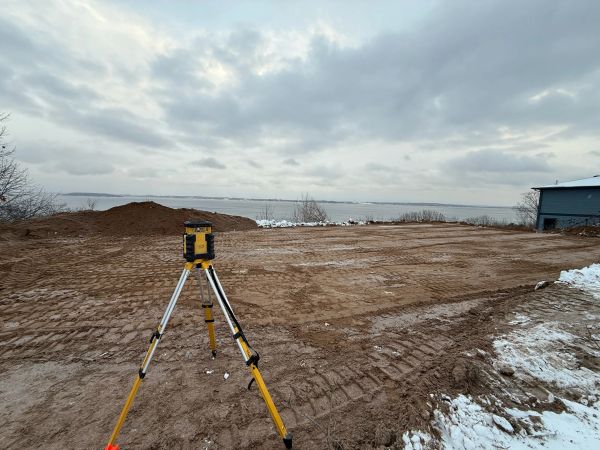 Surveying equipment on a cleared plot of land near water.