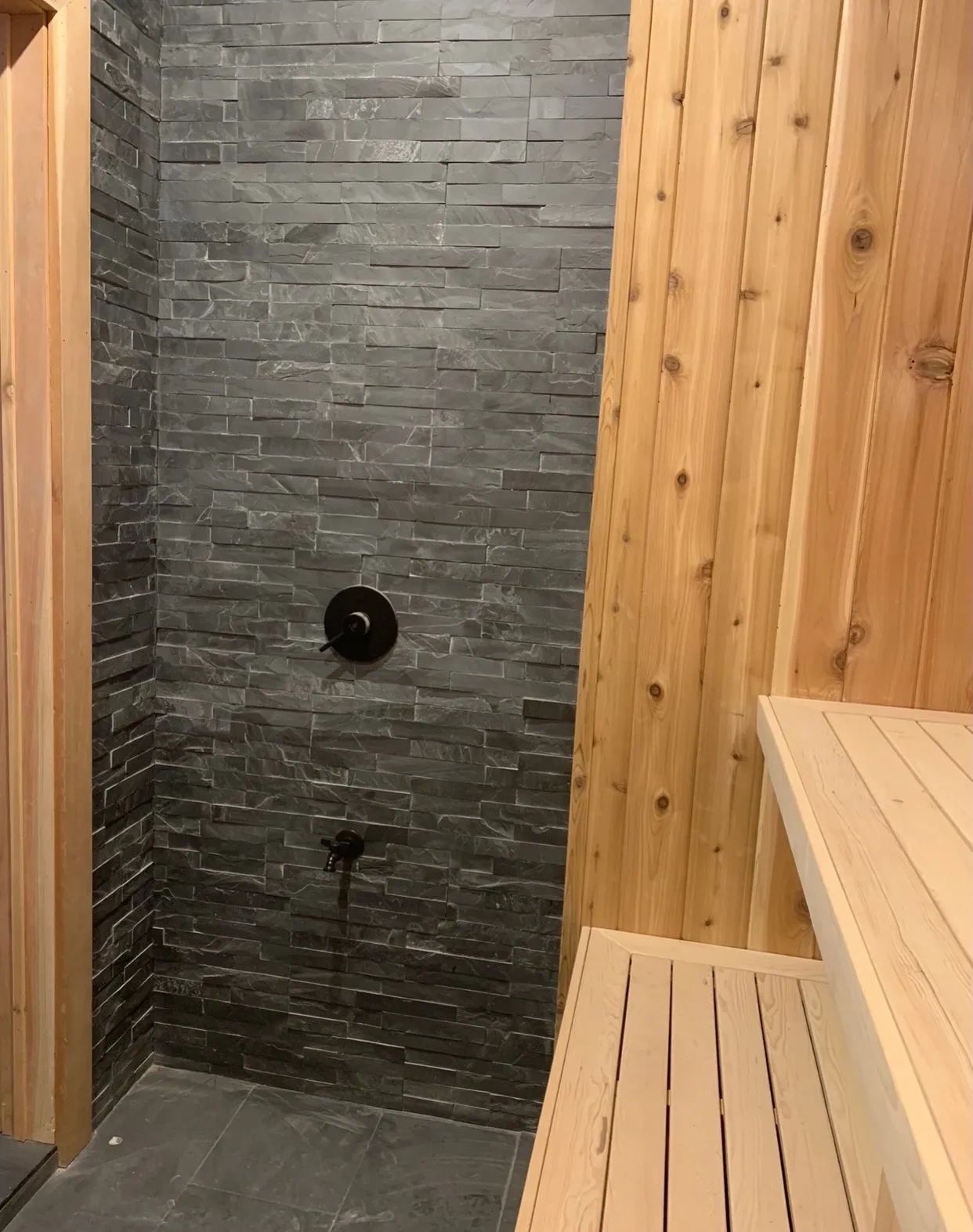 Rustic shower area with stone tiles and wooden bench.