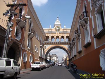 Historic street with an archway and colonial buildings under a blue sky.