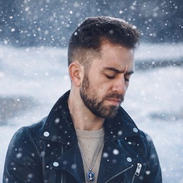 Man in a leather jacket standing in falling snow.
