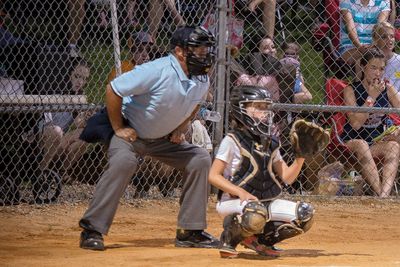girl at bat in front of catcher and umpire with fans sitting behind tall fence
