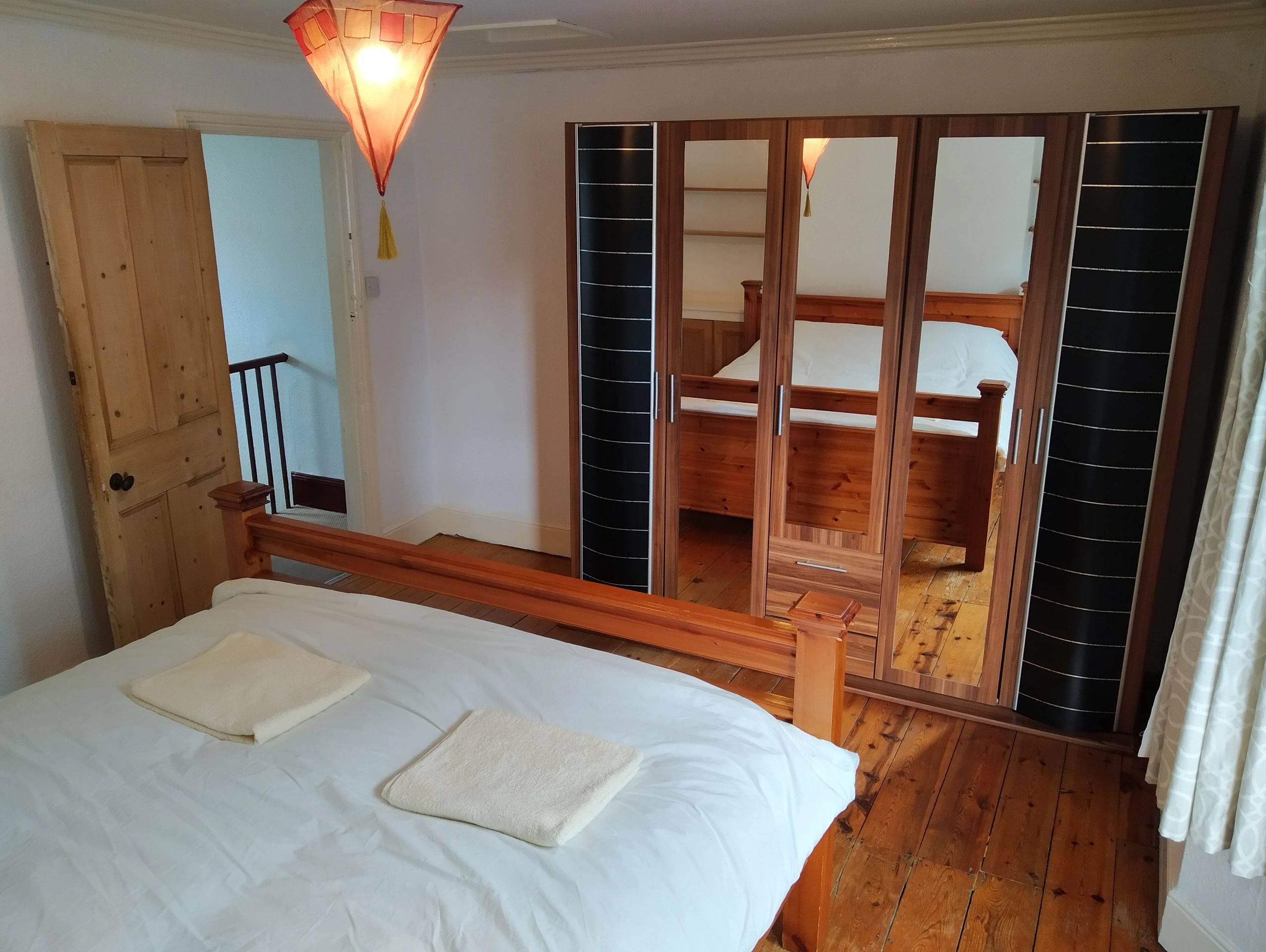 Large bedroom with made bed, wooden floorboards and full-length, mirrored wardrobe