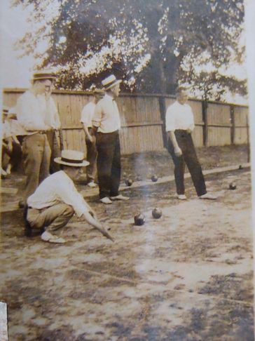 Men in vintage attire play a game of lawn bowling outdoors.