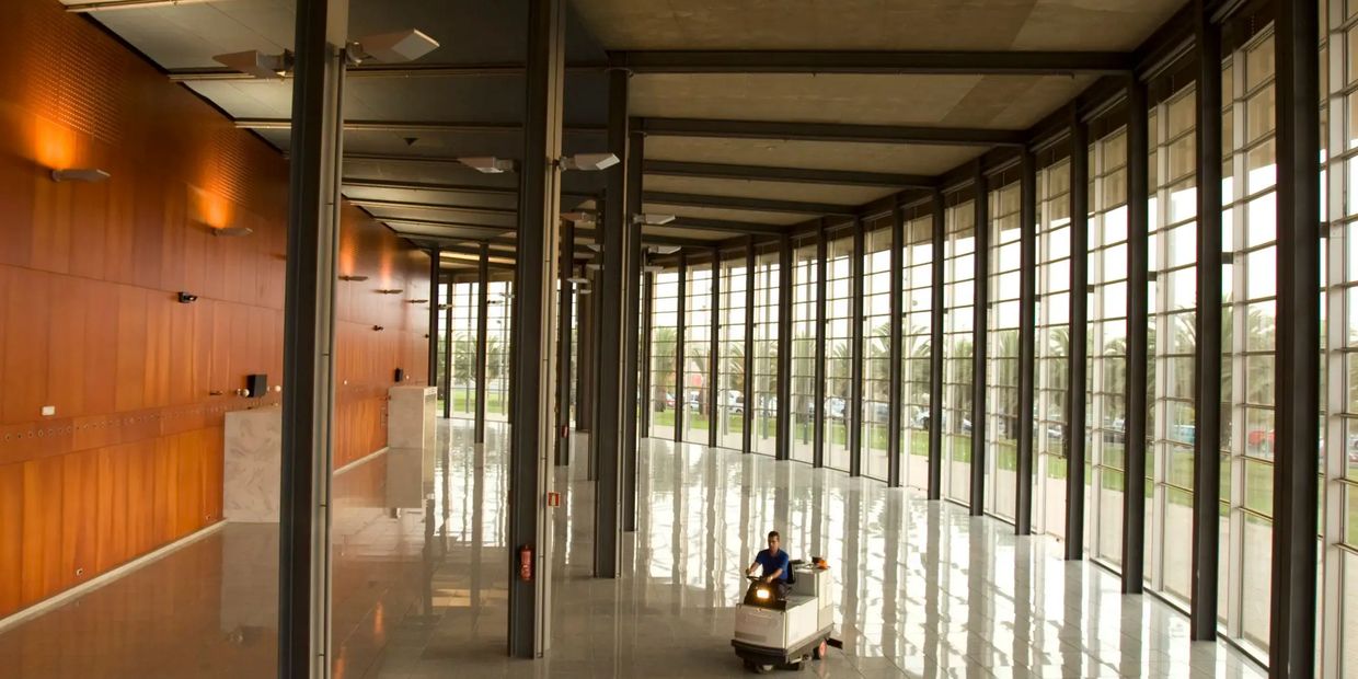 Person cleaning a spacious modern hall with large windows and reflective floors.