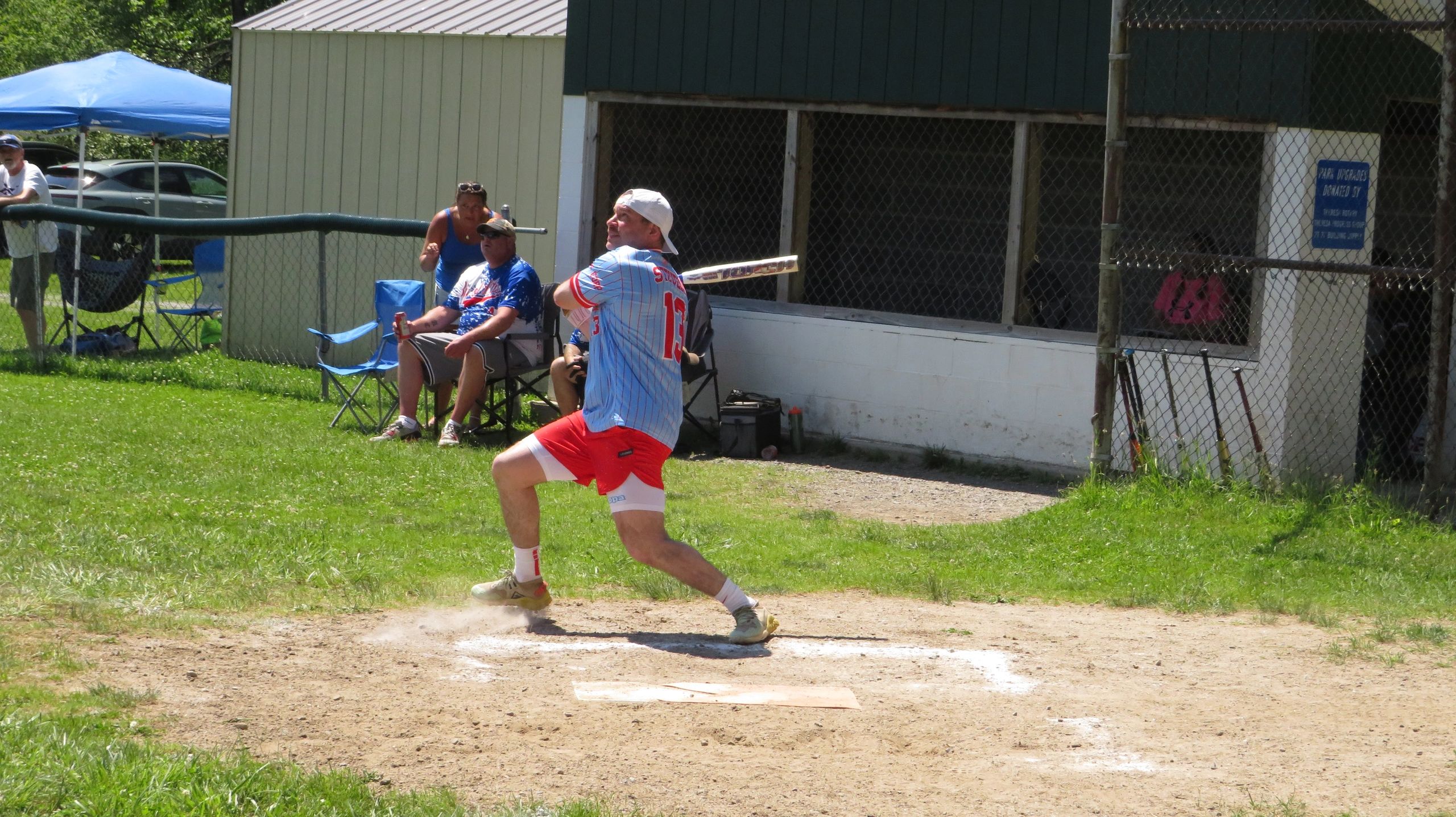 A baseball player swings the bat on a sunny day at a local field.