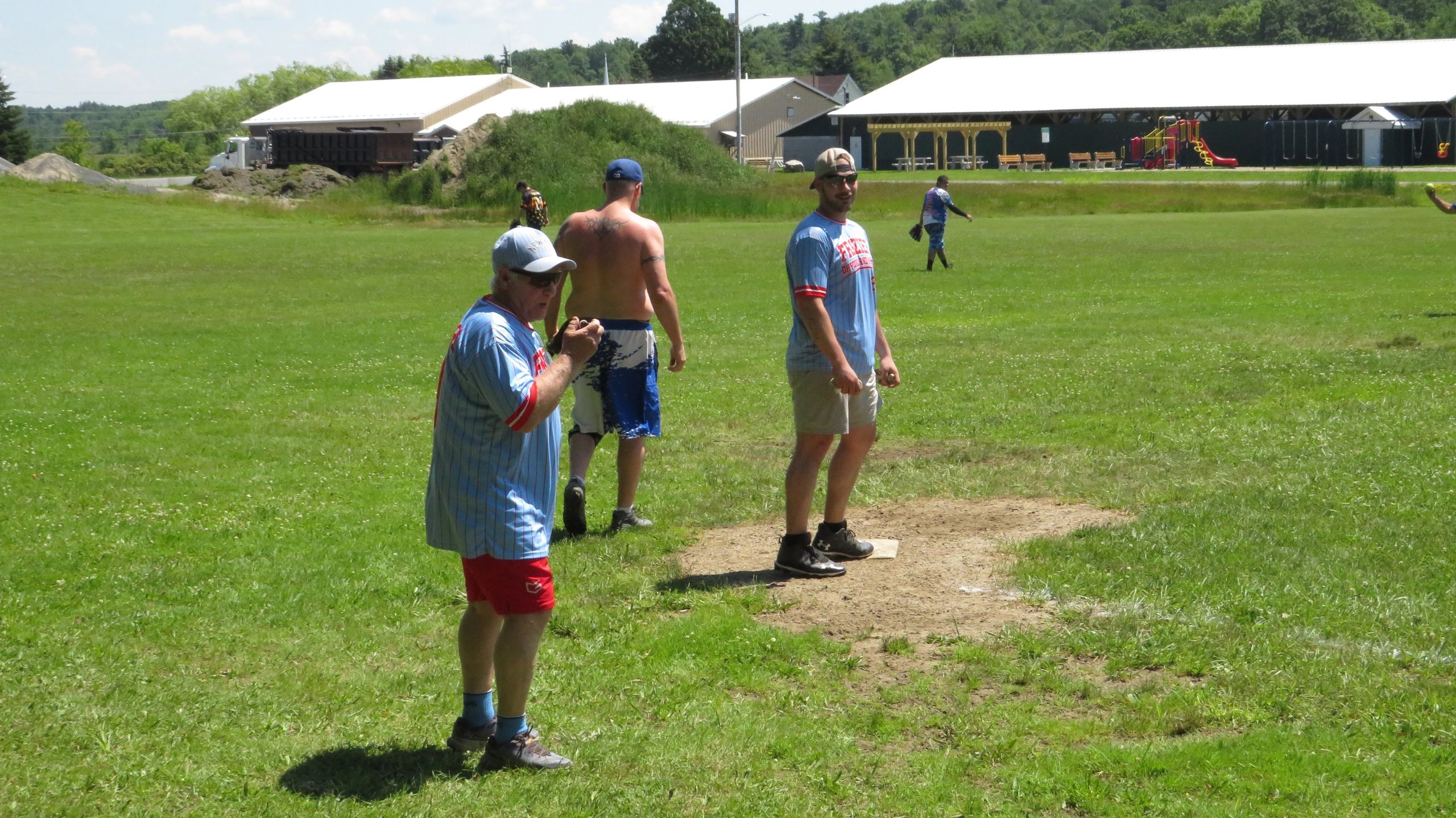 Men playing baseball on a sunny day in a grassy field.