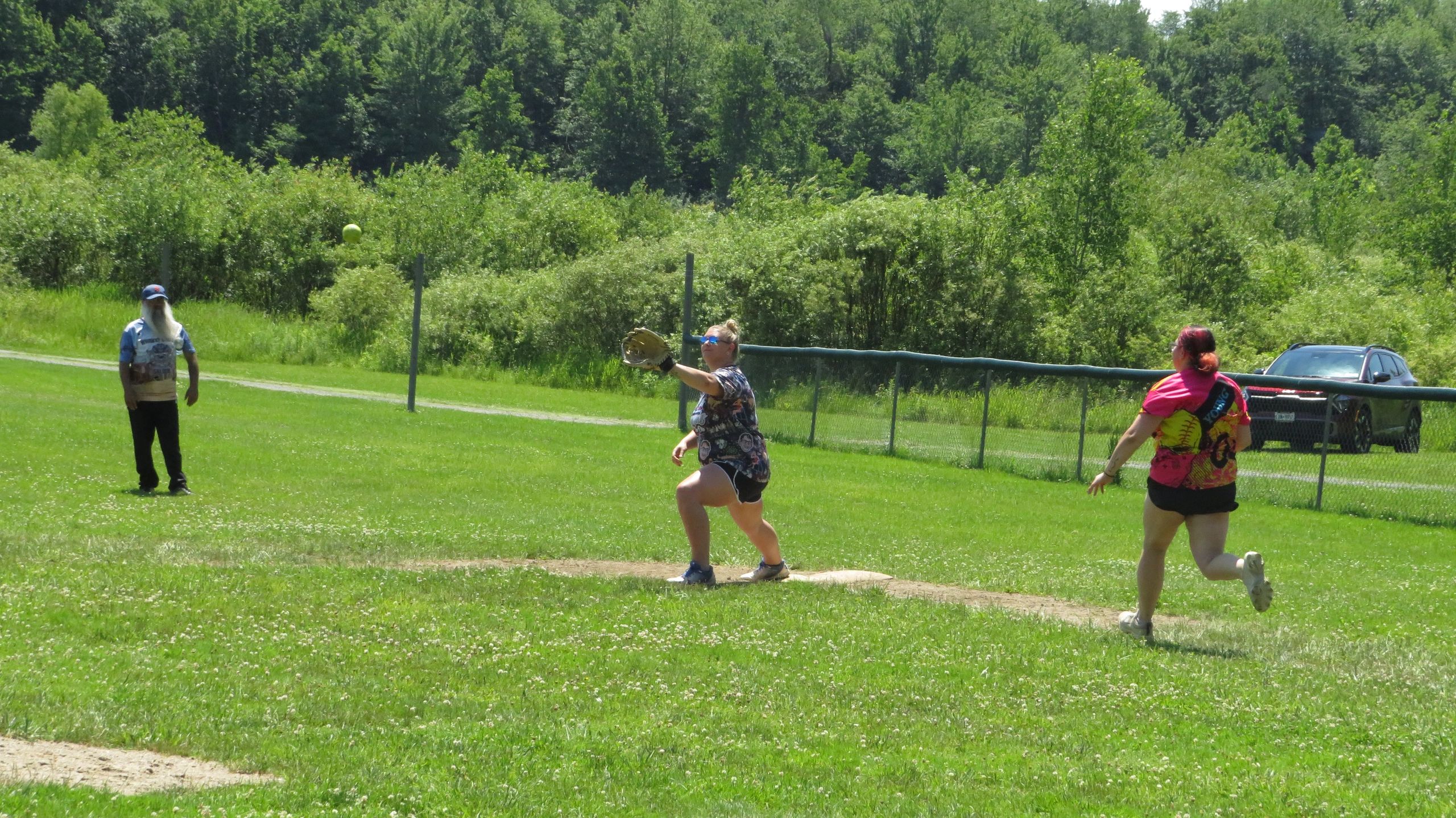 Three people playing softball on a sunny day in a green field.