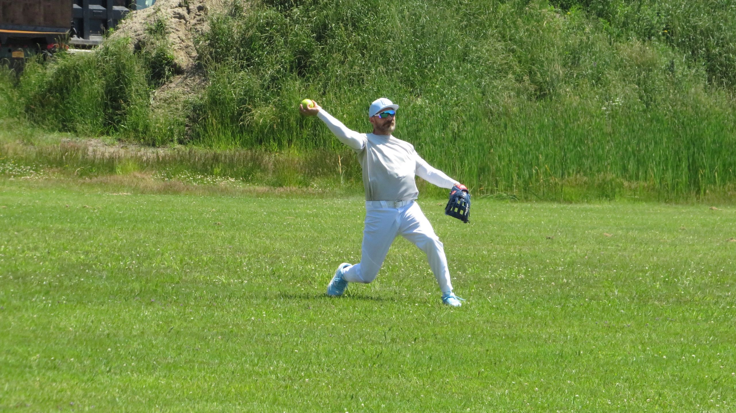 Man in white sportswear throwing a softball on a grassy field.