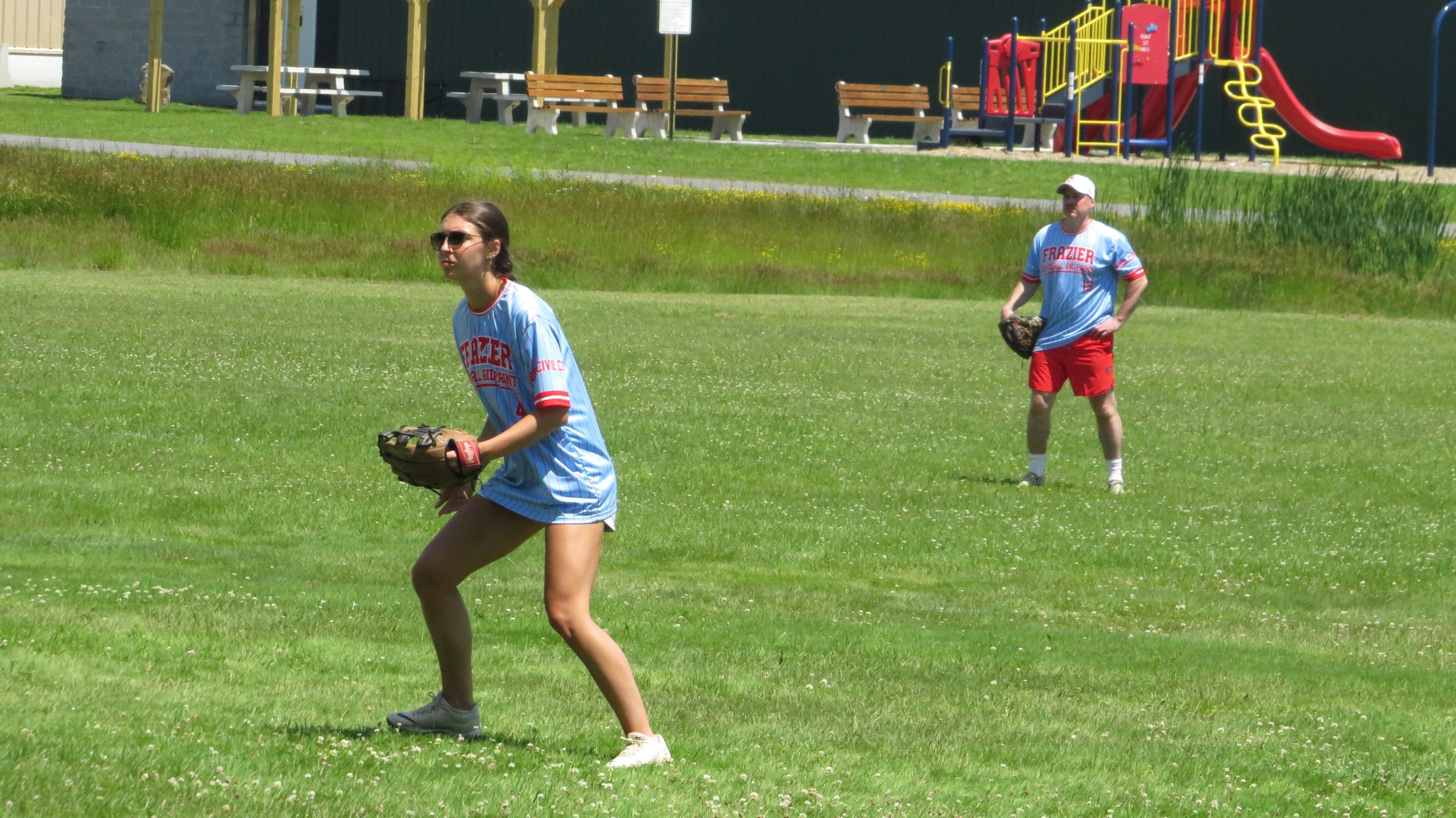 Two people in baseball gear playing on a grassy field near a playground.
