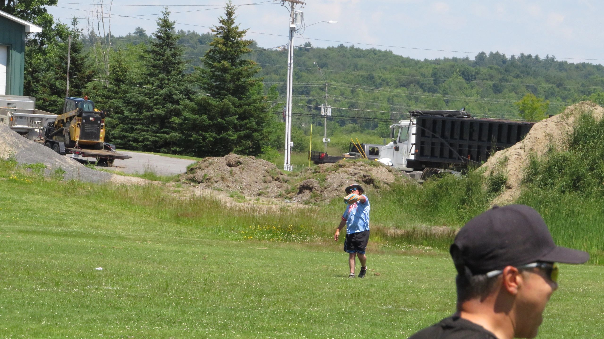 A man playing frisbee in a grassy field with construction equipment in the background.