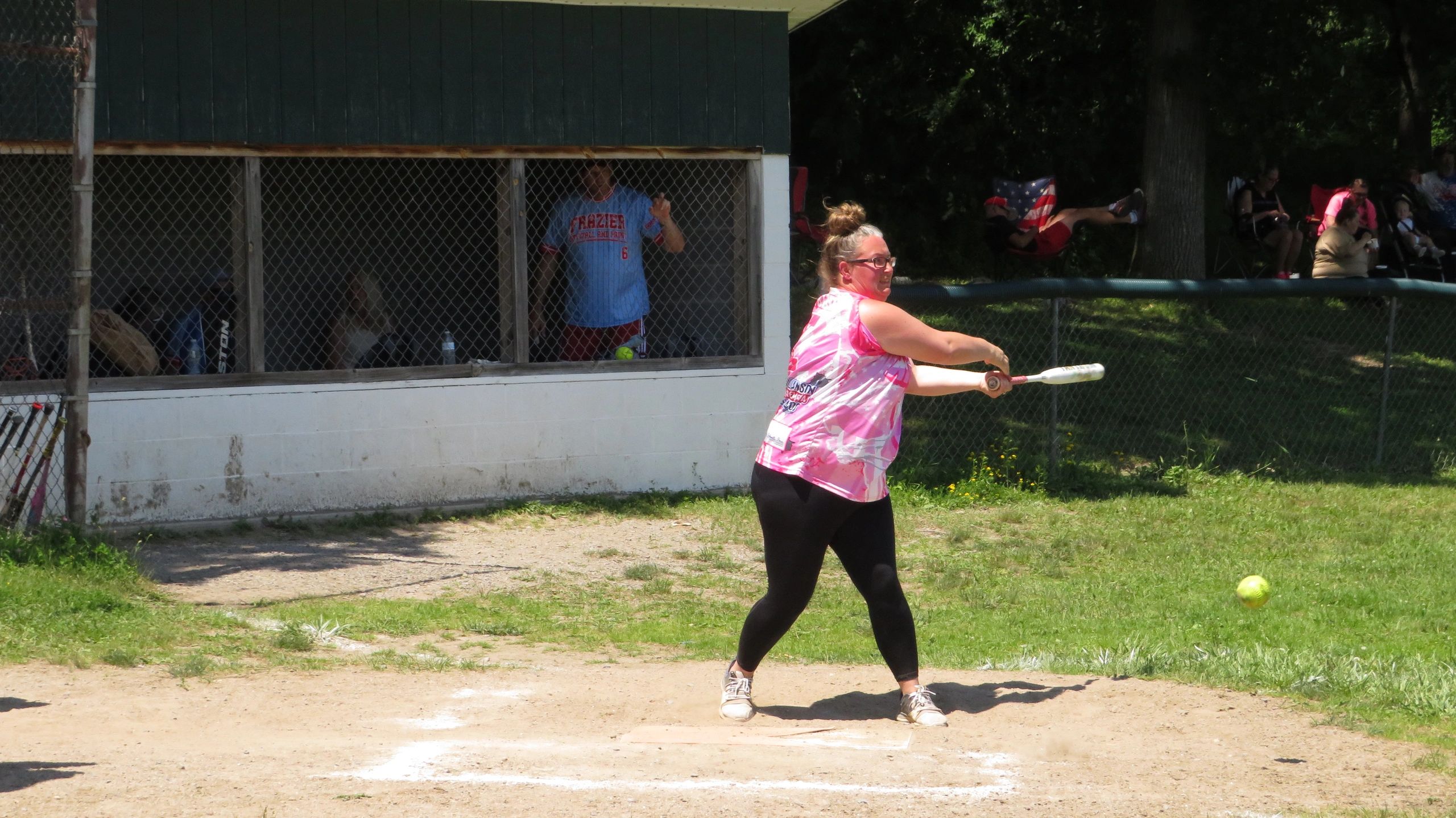 Woman in pink shirt hitting a softball on a sunny day.