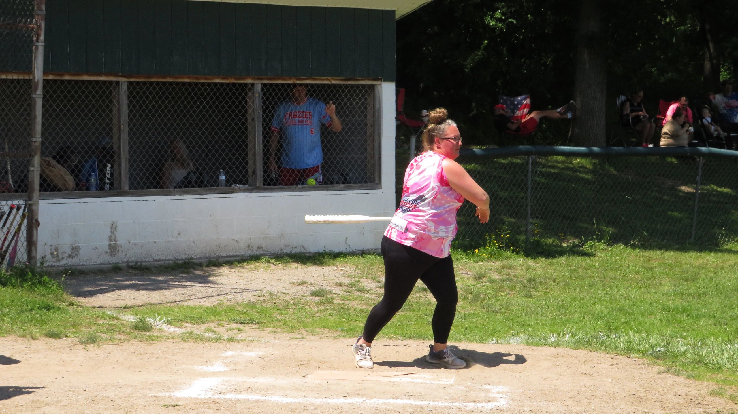 A woman playing softball with a bat in hand near a dugout.