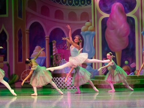 Ballet dancers perform on a colorful stage with a candy-themed backdrop.