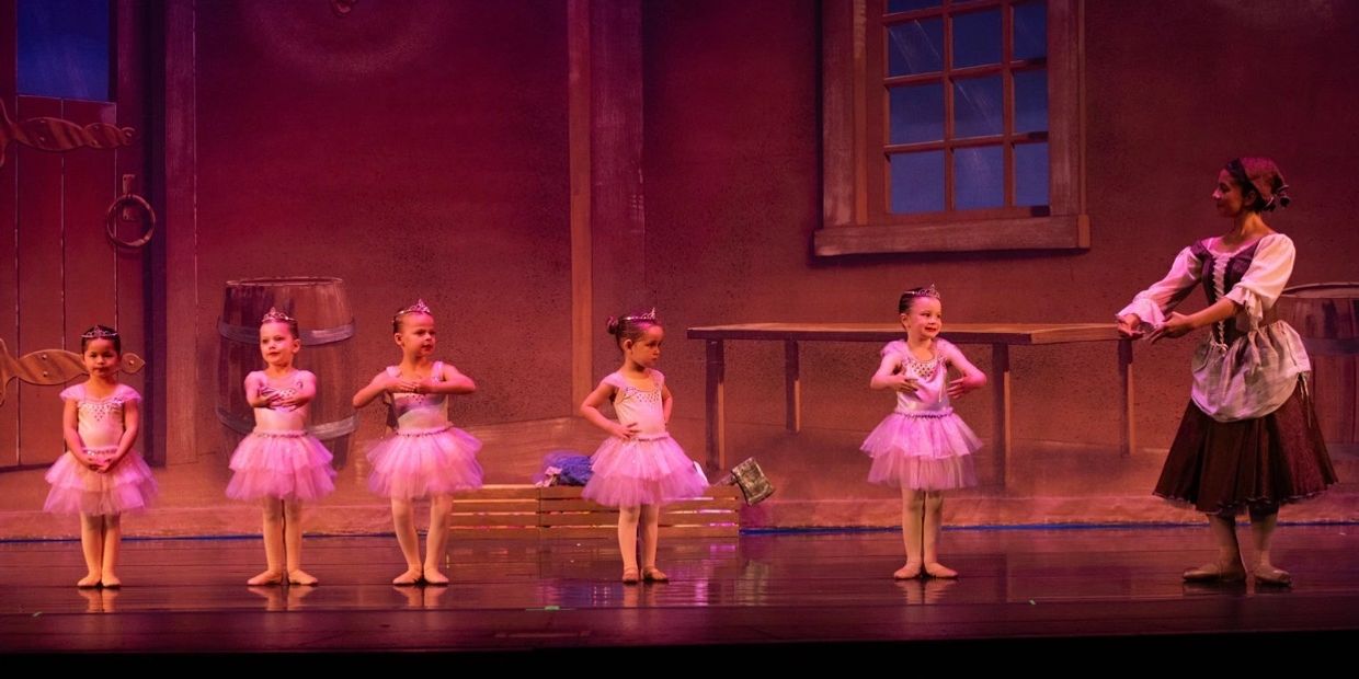 Five young ballerinas in pink tutus with their instructor on stage.