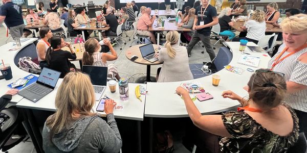 A group of adults engaged in a collaborative workshop or meeting around curved tables.