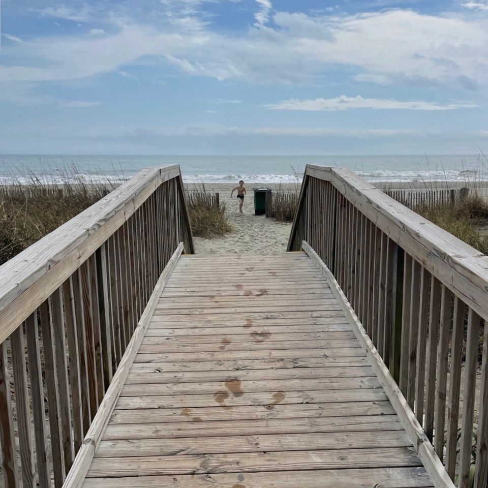 Wooden boardwalk leading to a beach with a child running in the sand.