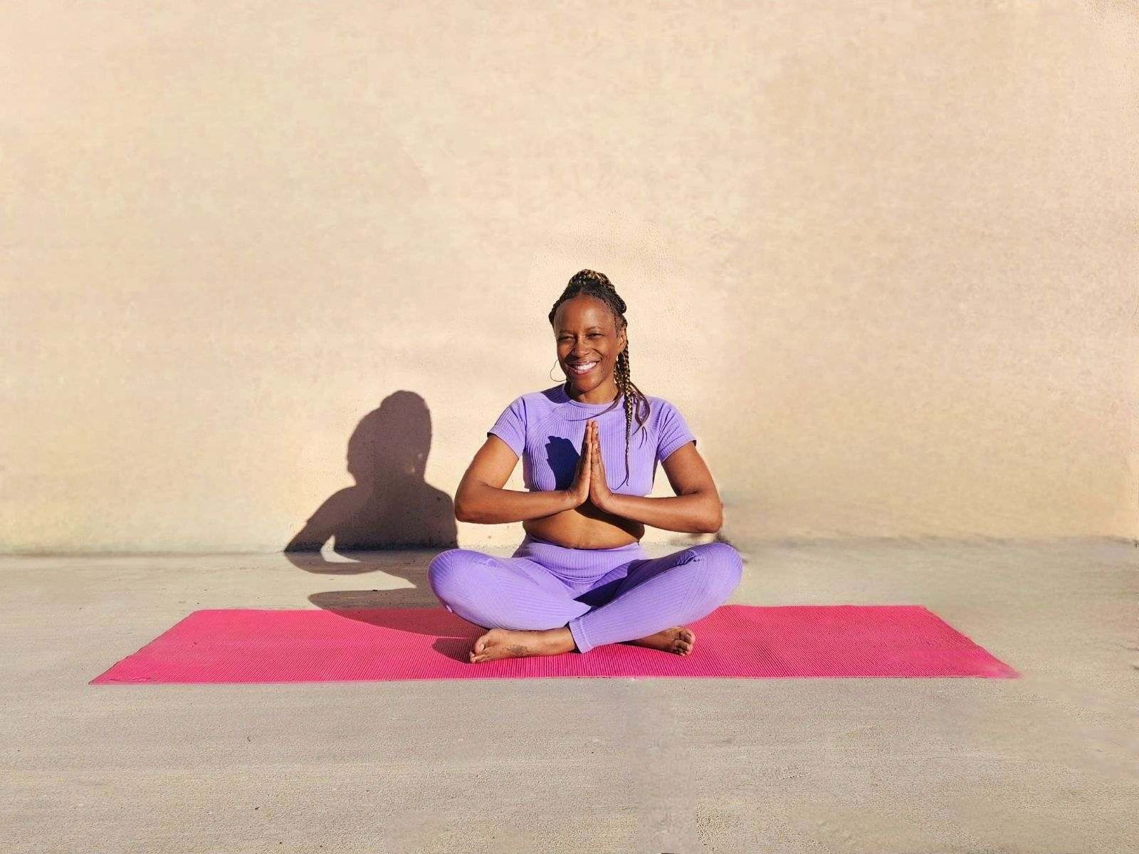 Woman wearing lavender yoga outfit sitting in easy pose with prayer hands.