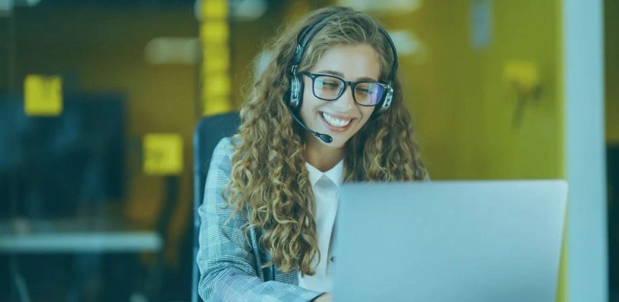 Woman with headset smiling at laptop.