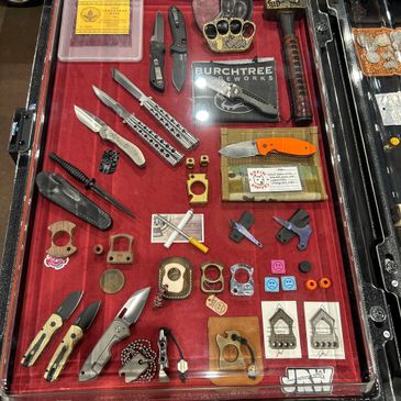 A display case filled with various knives, brass knuckles, and small tools.