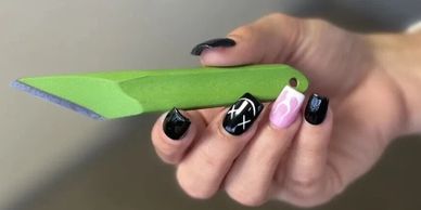 Hand holding a green utility knife with black and pink painted nails.
