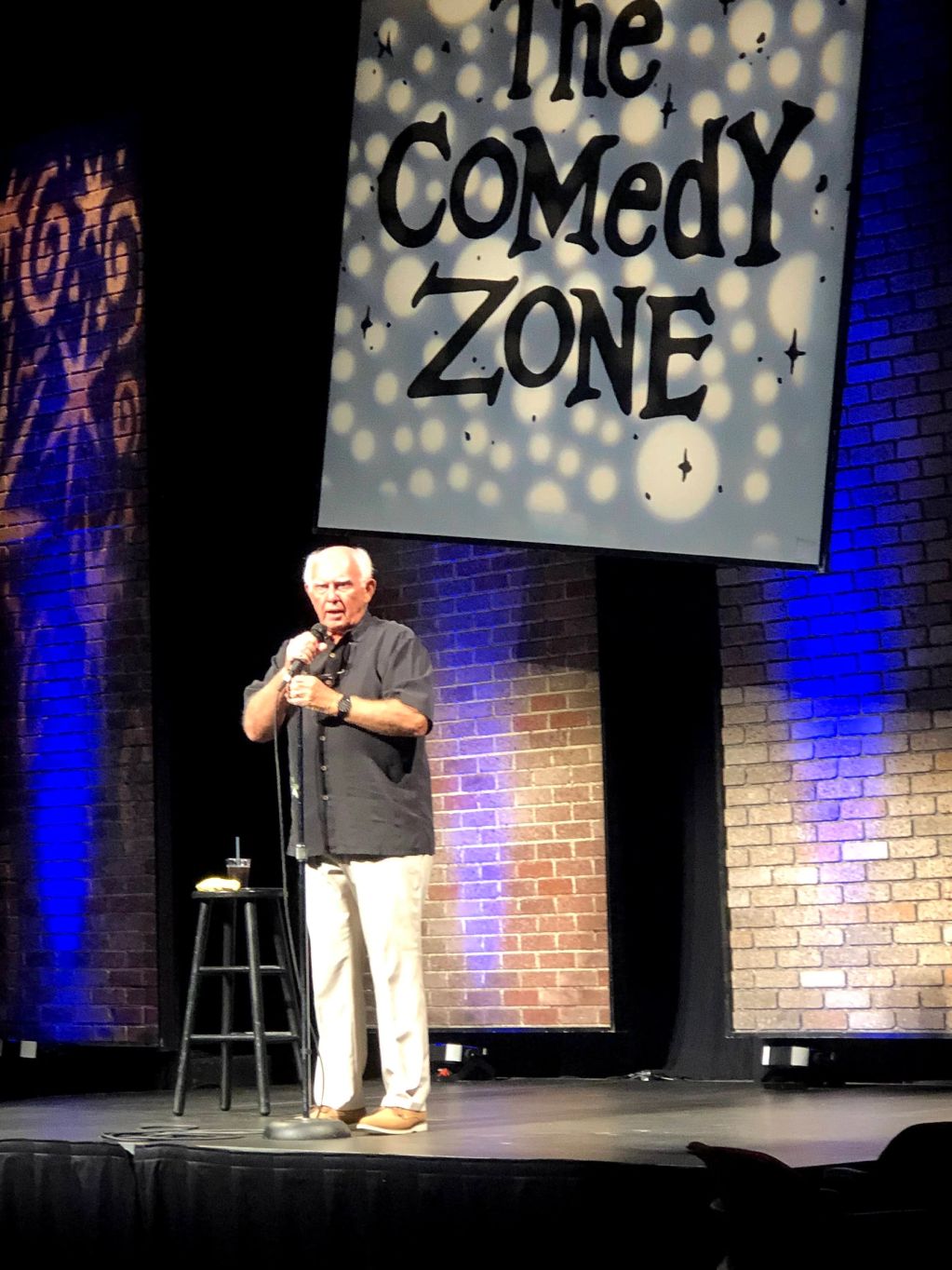 An elderly man performing stand-up comedy on stage.