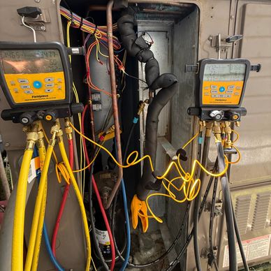 Two HVAC diagnostic gauges connected to an air conditioning unit with colorful hoses.