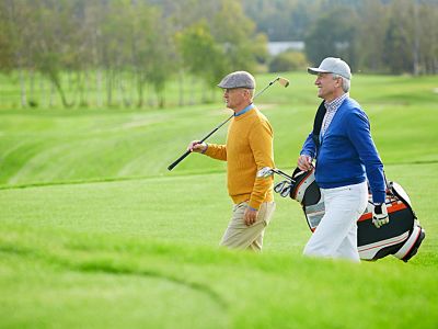 Two elderly men walking on a golf course with golf clubs.