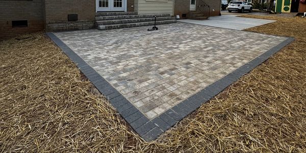 Newly constructed stone patio with a dark border and surrounding straw mulch.
