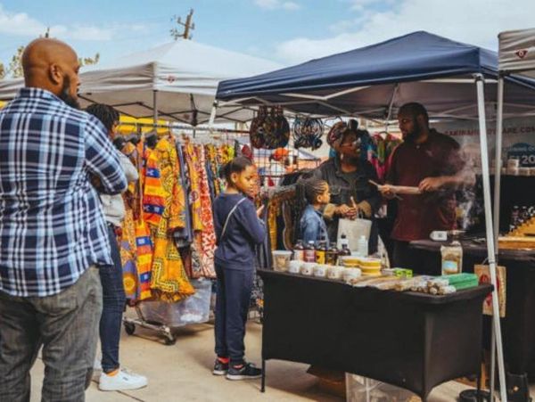 People shopping at an outdoor market with vibrant clothing and food stalls.