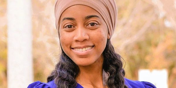 Woman smiling outdoors with a headwrap and blue dress.