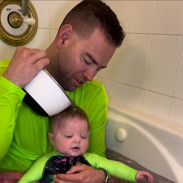 A man pouring some water on the head of a baby.