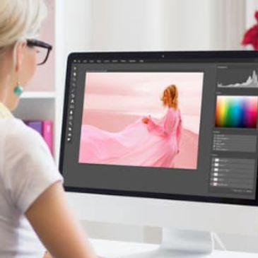 A woman editing a photo of a girl in a pink dress on a desktop computer.