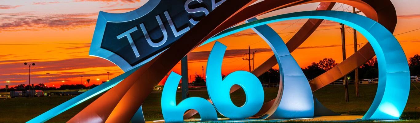 Colorful Tulsa Route 66 sign illuminated against a vibrant orange sunset sky.