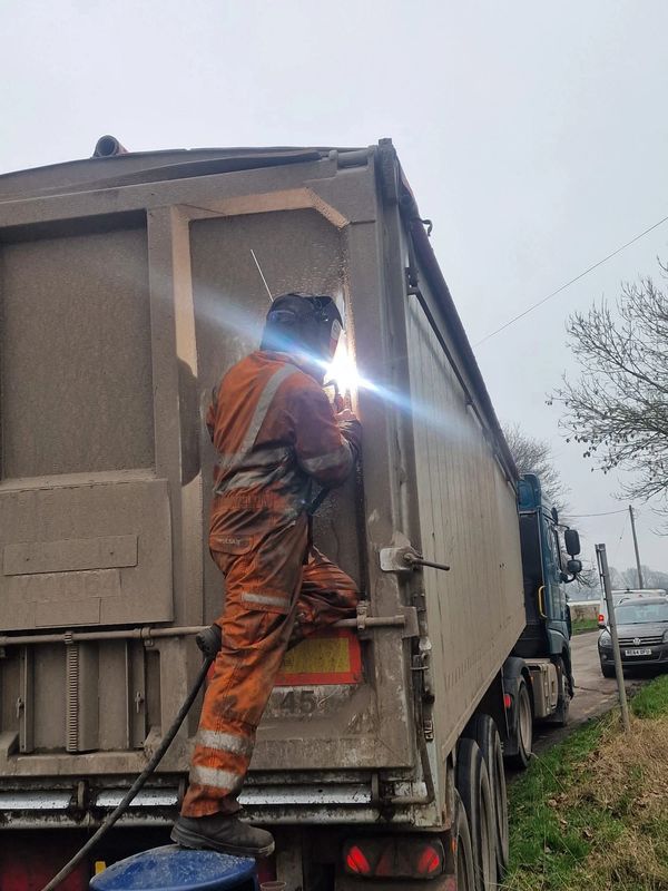 Worker welding on the back of a large truck in a safety suit.