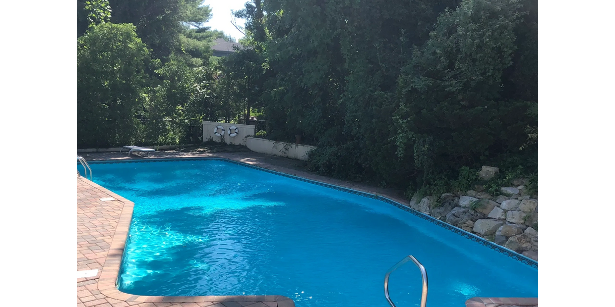 Outdoor swimming pool surrounded by trees and a brick patio.
