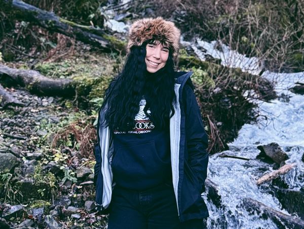 Smiling woman in winter clothing by a flowing stream.