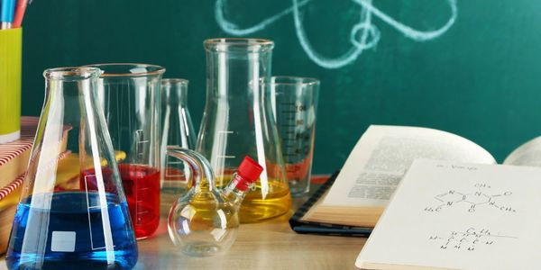 A chemistry set consisting of half-full beakers next to two open books and a green blackboard.