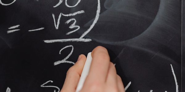 A person writing math on a blackboard with chalk.
