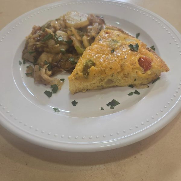 Porción de frittata con vegetales y guarnición en plato blanco.