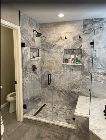 Modern marble-tiled shower with glass door and built-in shelves.