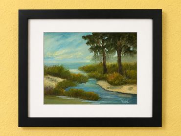 Framed painting of a serene riverside landscape with trees and a blue sky.