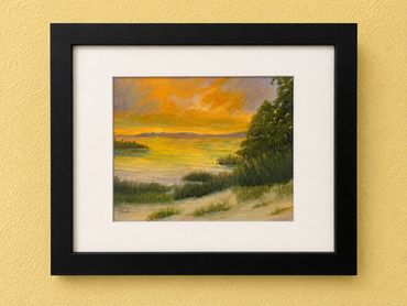 Framed painting of a sunset over a lake with trees and grass.