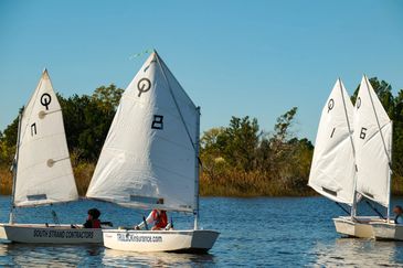 Small sailboats with white sails on a calm lake under clear blue sky.