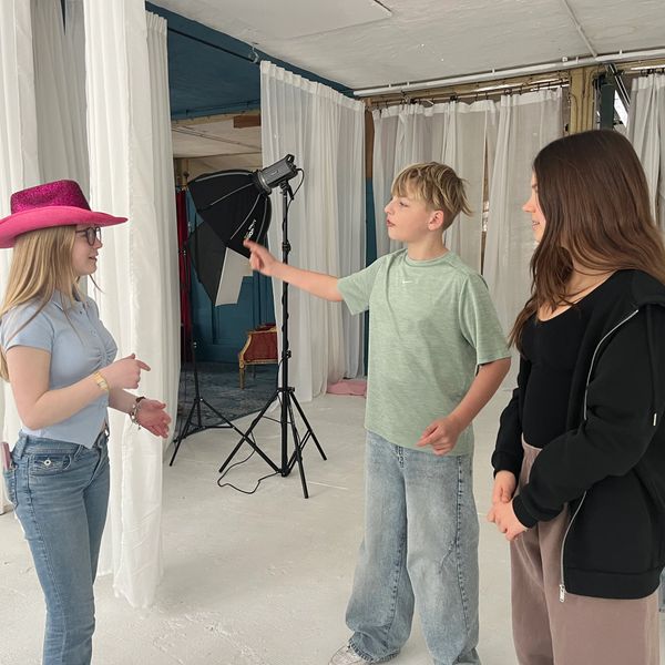 Three young people interacting in a studio setting with white curtains and photography equipment.