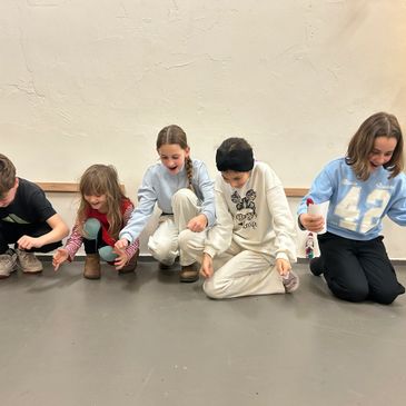 Five children sitting on the floor, focused on an activity with small cups.