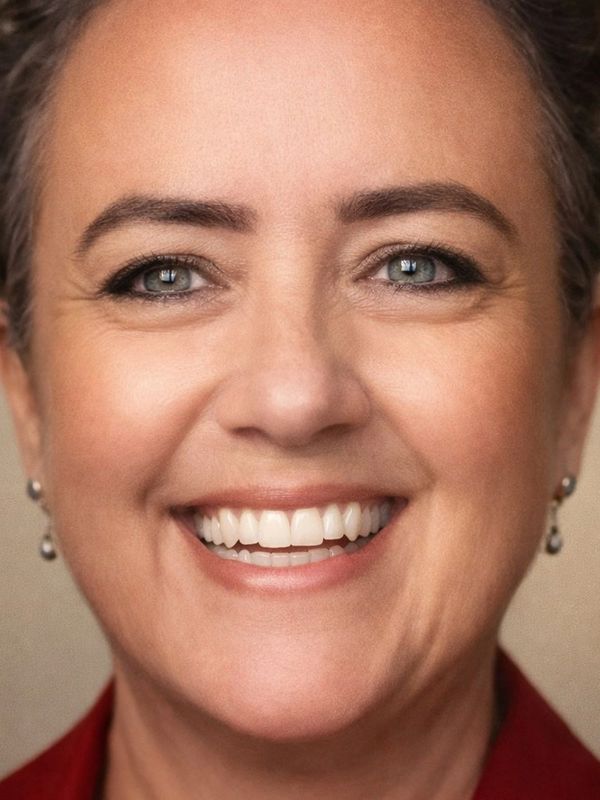 Close-up of a smiling woman with clear blue eyes and pearl earrings.